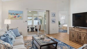 Un salon moderne avec une table basse en verre, un canapé agrémenté de coussins à motifs, un meuble TV en bois et un ventilateur de plafond.