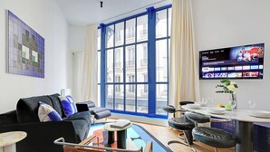Una sala de estar moderna con un ventanal grande, un televisor de pantalla plana, un sofá, una mesa de centro y un comedor con taburetes de bar.