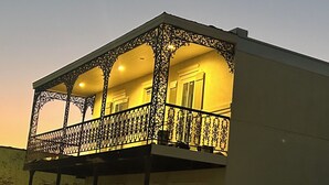 A two-story building with a balcony featuring ornate metal railings and a warm light.