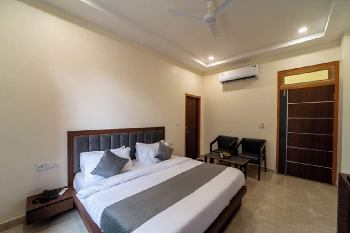A hotel room with a large bed, a desk, a chair, an air conditioning unit, and a ceiling fan.