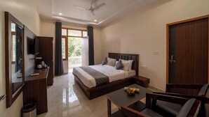 A modern hotel room with a large bed, a desk, a chair, a TV, and a balcony with curtains. - Joy Bagh Resort  (Pushkar)
