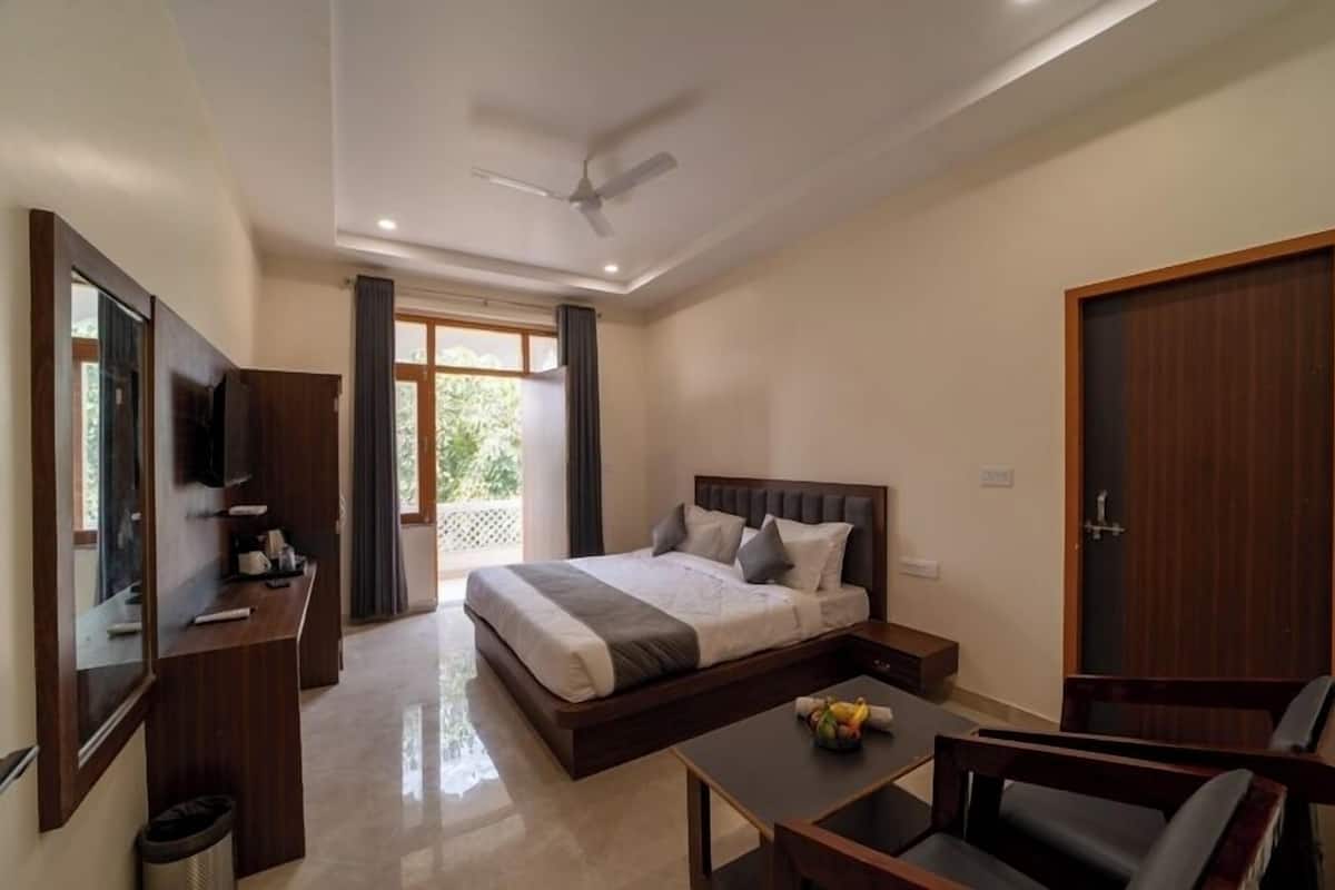 A modern hotel room with a large bed, a desk, a chair, a TV, and a balcony with curtains.