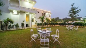 A courtyard with a dining area, white outdoor furniture, and a building with traditional architecture. - Joy Bagh Resort  (Pushkar)