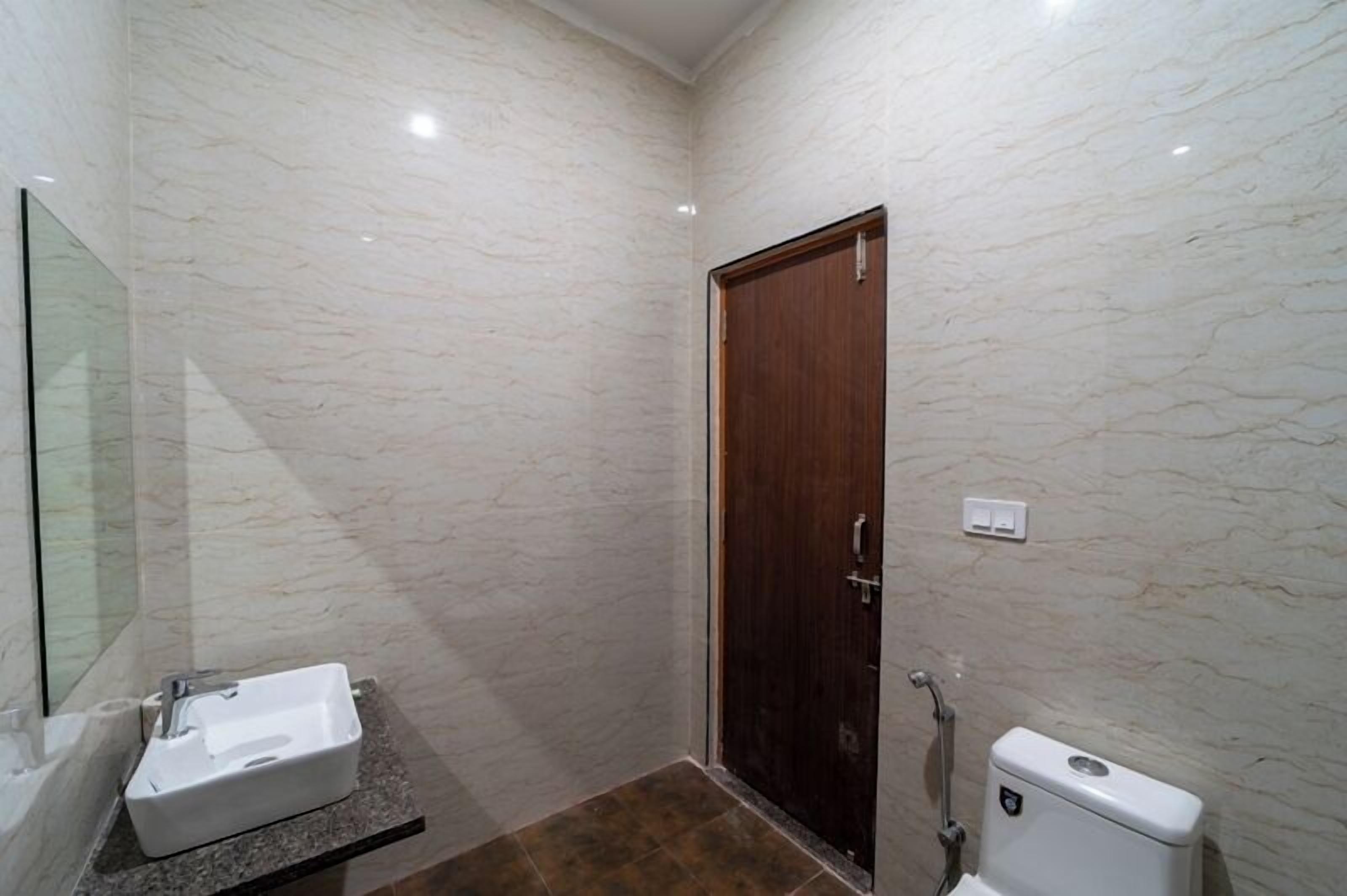 A bathroom with a marble wall, a wooden door, a white sink, and a toilet.