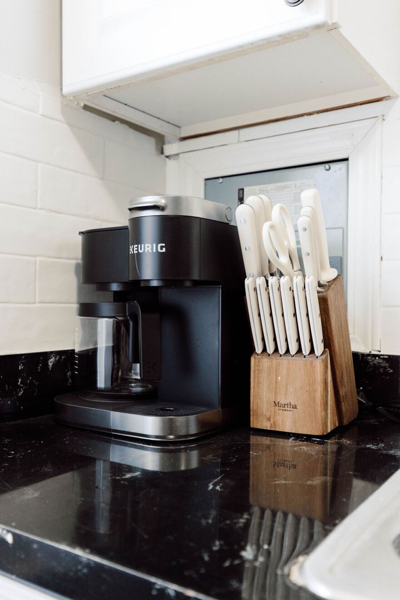 Una cafetera Keurig negra sobre una encimera negra con un bloque de cuchillos Martha.