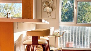 A modern kitchen with a herringbone wood floor, a bar area with stools, and a view of trees through large windows. - St Albans Gem: Stylish Flat, Balcony, Easy Commute (St Albans)