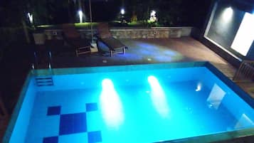 A rectangular swimming pool with a tiled deck and a stone wall surrounding it.