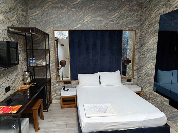 A hotel room with a marble-patterned wall, a bed with white linens, a desk with a coffee maker, a mirror, and a TV on a shelf. - MELISA SUIT RESIDENCE (Istanbul)