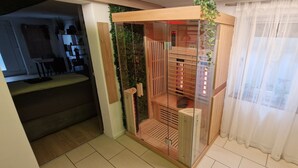 Un salón moderno con un separador de vidrio, una sauna de madera y una pared verde con plantas.