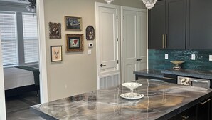 Una cocina moderna con armarios oscuros, una isla de mármol e iluminación colgante.