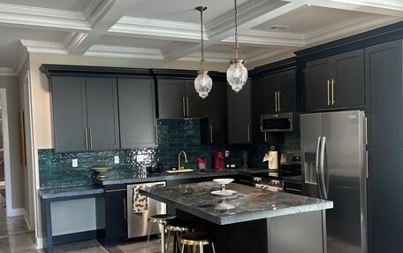 A modern kitchen with dark cabinetry, a central island, bar stools, and a chandelier.