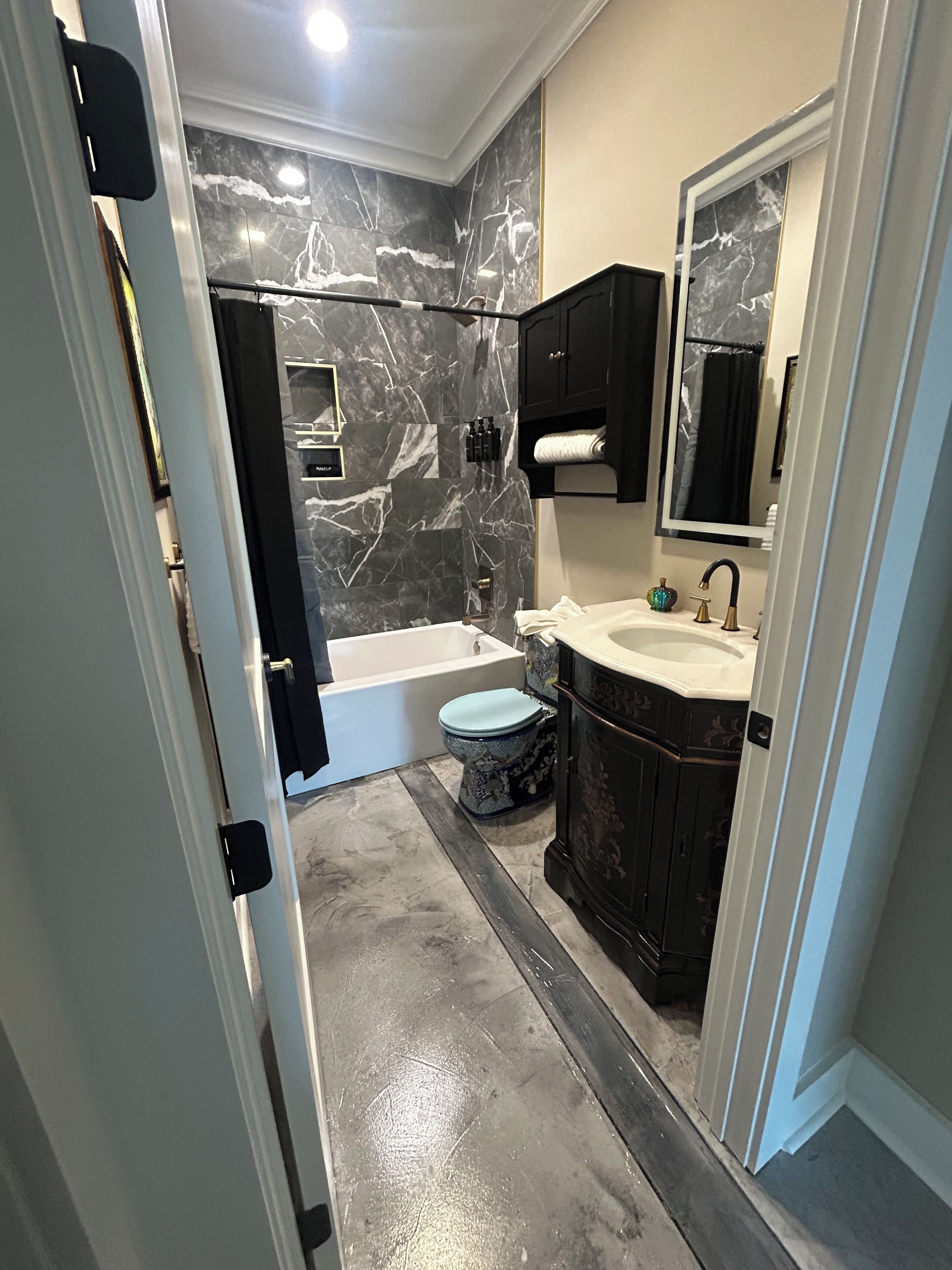 A bathroom with a marble wall, a bathtub, a toilet, and a sink with a mirror.