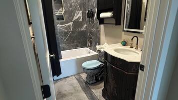 A bathroom with a marble wall, a bathtub, a toilet, and a sink with a mirror.