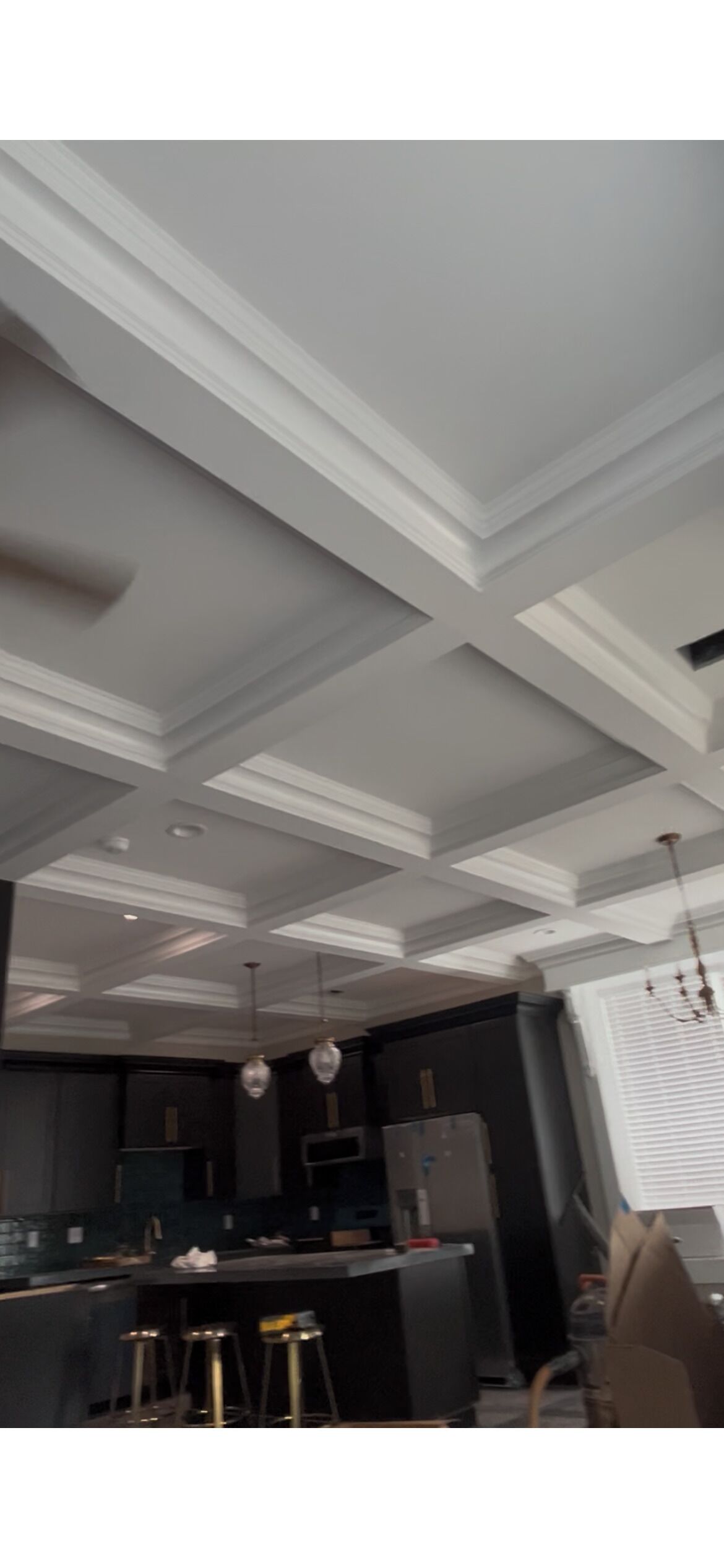 Una cocina moderna con encimera oscura, taburetes de bar y techo blanco con molduras decorativas.