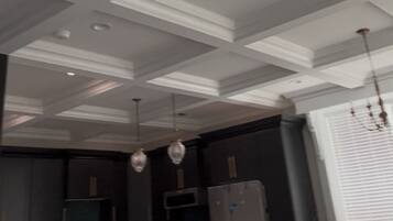 Una cocina moderna con encimera oscura, taburetes de bar y techo blanco con molduras decorativas.