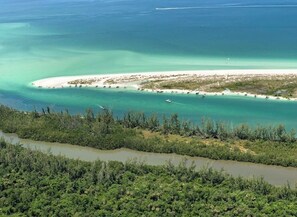 An aerial view of a coastal area with a beach, boats, and dense vegetation.