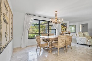 A dining area with a large table and chairs, a chandelier, and a view through large windows.