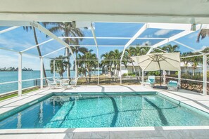A pool area with clear blue water, surrounded by a white fence and palm trees, overlooking a body of water.