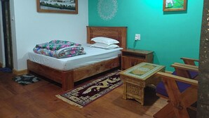 A bedroom with a wooden bed, a nightstand, a small table, and a chair. There is a picture on the wall and a rug on the floor.