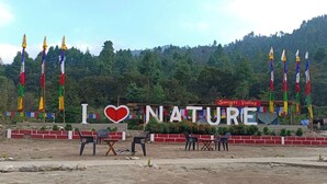 A sign with "I ♥ NATURE" and "Sangti Valley" in a rural setting with flags and a mountainous backdrop.