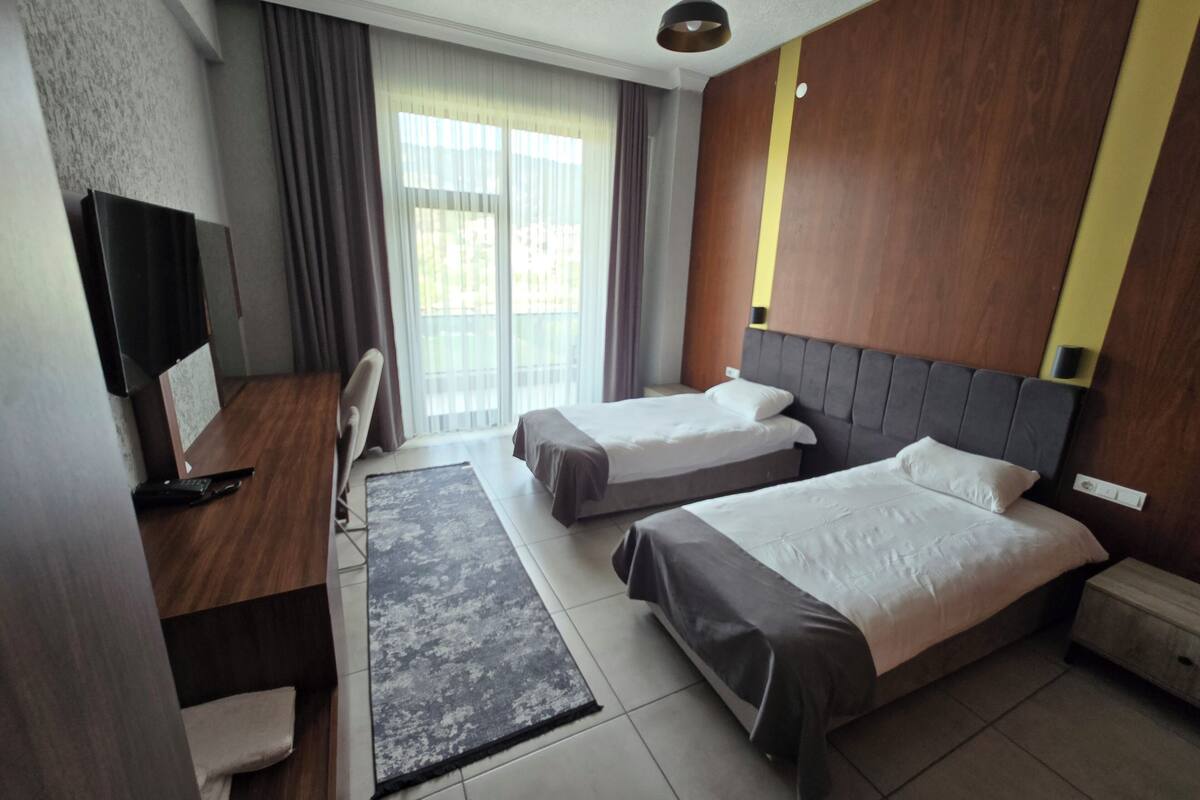 Een hotelkamer met twee bedden, een bureau, een stoel, een televisie en een groot raam met gordijnen.