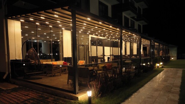 An outdoor dining area with tables and chairs, a covered seating area, and a glass enclosure with interior lighting.