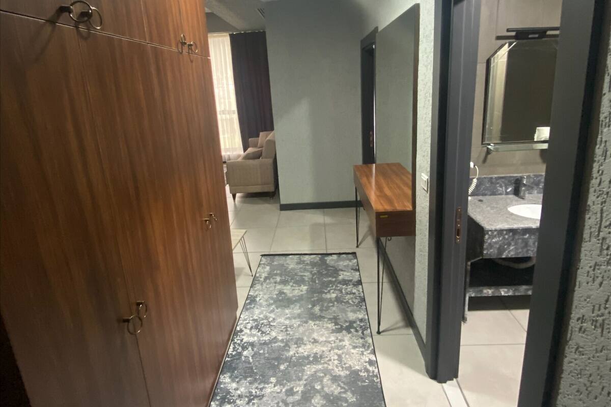Een gang met een houten garderobe, een spiegel, een tafeltje en een badkamer die door een geopende deur zichtbaar is.