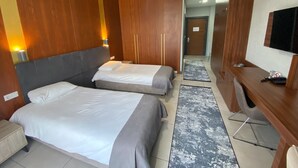 A hotel room with two beds, wooden walls, a desk, a television, and a hallway leading to another room.