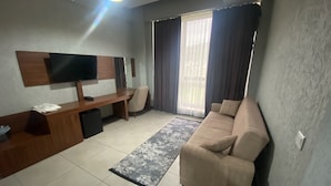 A modern living room with a sofa, a desk, a TV, and a large window with curtains.
