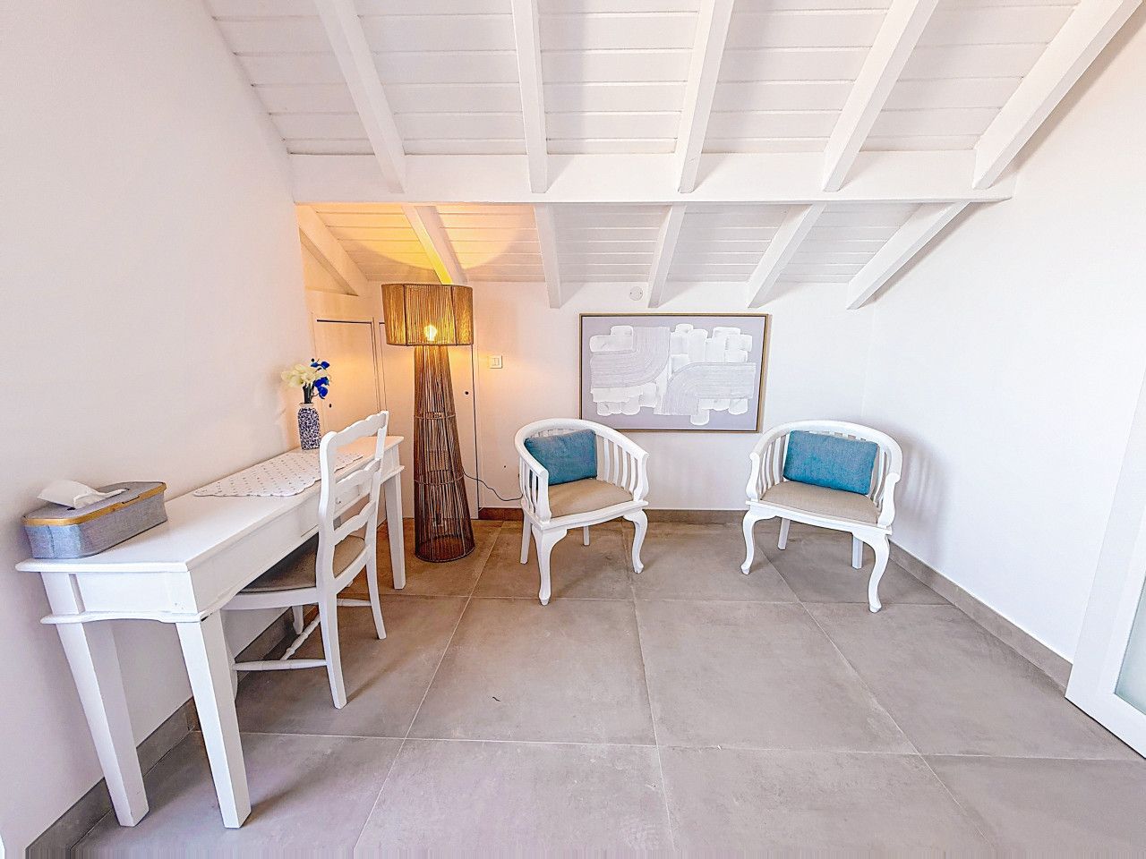 A room with a white desk, two white chairs, a lamp, and a framed picture on the wall.