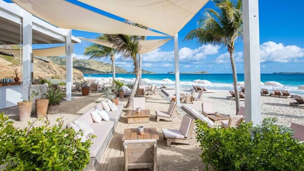 Eine Strandlounge mit Sitzgelegenheiten im Freien, Palmen und Blick auf den Ozean.