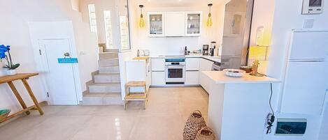 A modern kitchen with white cabinets, a built-in oven, and a refrigerator. There is a wooden stool and a woven basket on the floor.