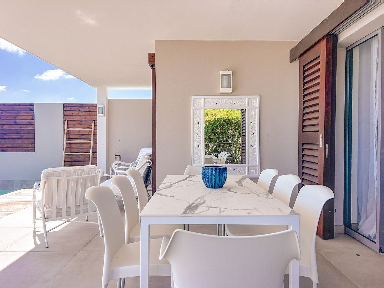 A dining area with a marble table, white chairs, and a blue vase centerpiece.