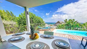 Ein Essbereich mit Blick auf Pool und Meer, umgeben von üppiger Vegetation.