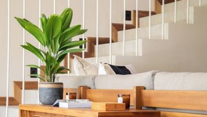 Una sala de estar moderna con un banco de madera, una planta en maceta y una escalera al fondo.