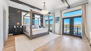 A spacious bedroom with a four-poster bed, a large window with a view, and a modern chandelier. - Luxury Beach House - Rooftop Decks with 360° Ocean & Bay Views, Pool, Elevator (Somers Point)