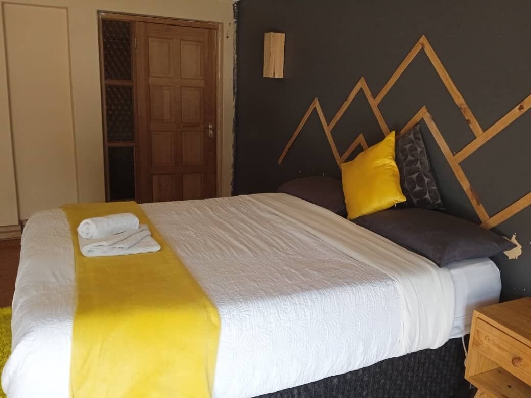 A neatly made bed with a white and yellow bedspread, a wooden headboard with geometric patterns, and a nightstand with a wooden drawer.