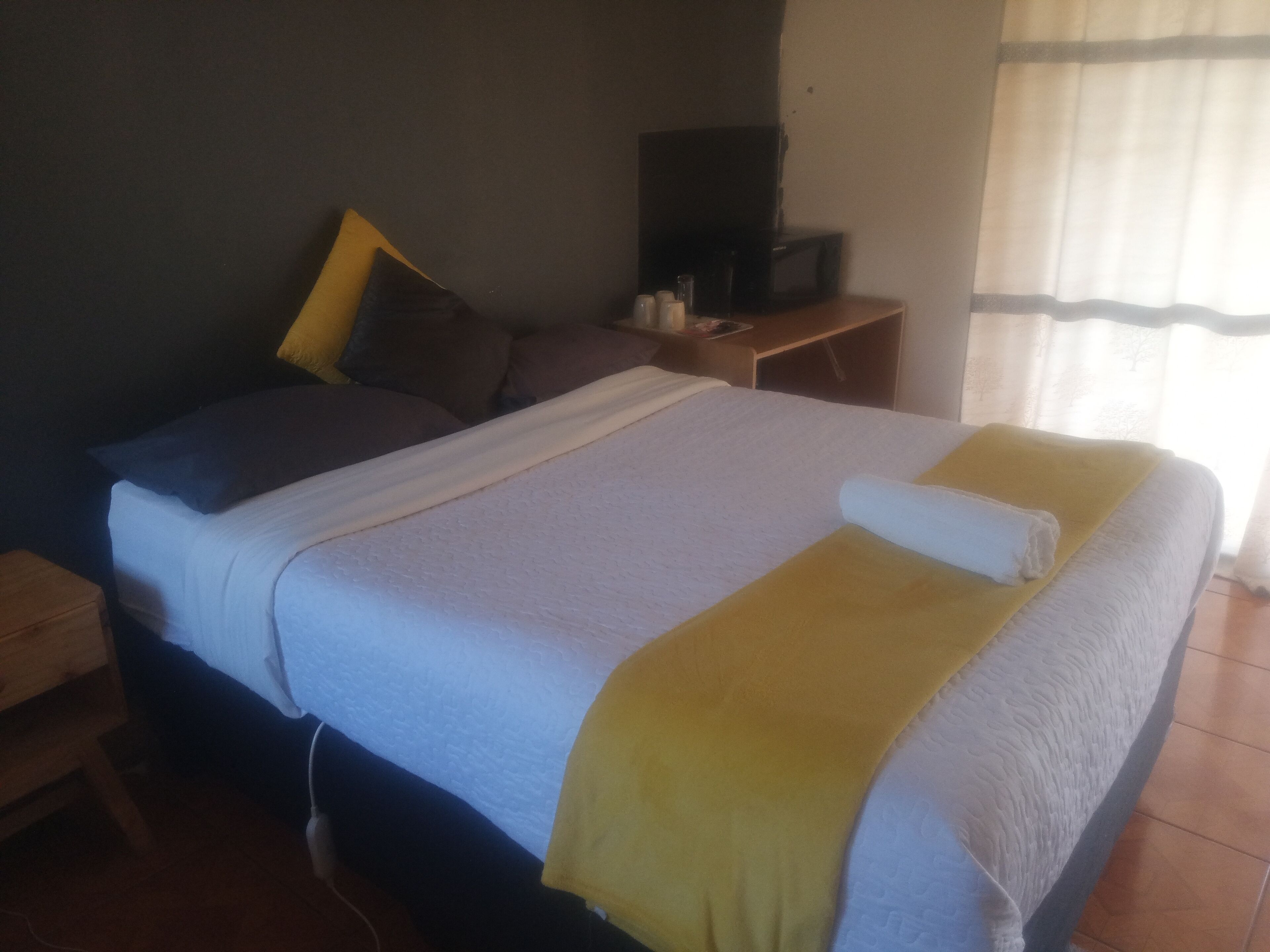 Habitación estándar de hotel con cama, televisor sobre una mesita auxiliar y ventana con cortinas.