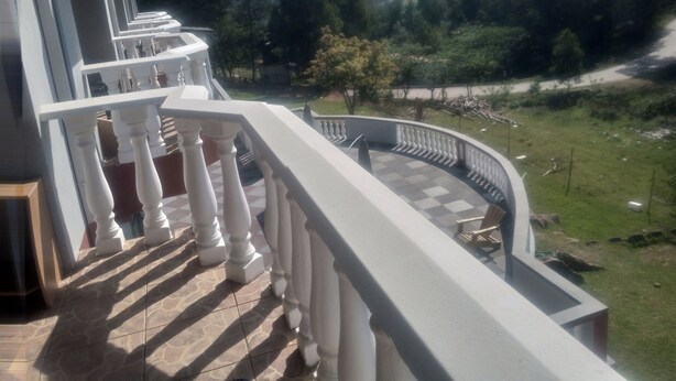 A balcony with white balustrades overlooking a scenic landscape with trees and hills. - Haven guesthouse nkoyoyo (Mbabane)