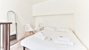 Habitación de hotel con una cama grande, una mesita de noche, una silla, un espejo y un pequeño escritorio con lámpara.