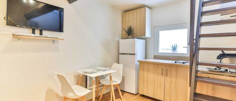 A compact kitchen with a wooden table and chairs, a built-in TV, and a refrigerator.
