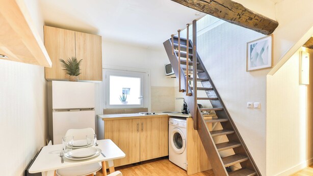 Una cocina compacta con armarios de madera, lavadora y comedor con mesa y sillas.