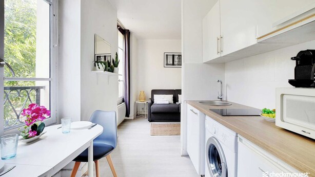 Cocina compacta con lavadora, comedor con mesa y sillas, y vista al exterior a través de una ventana.