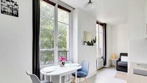 Una habitación moderna y bien iluminada con una mesa de comedor, dos sillas, una mesita auxiliar, un sofá y un ventanal con vistas a zonas verdes.