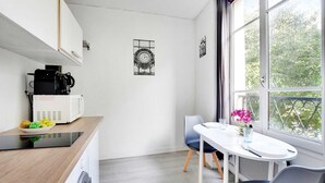 Une cuisine moderne équipée d’une machine à café, d’un four à micro-ondes et d’un panier à fruits. On y trouve également un coin repas avec une table et des chaises, ainsi qu’une fenêtre donnant sur la verdure.