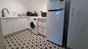 A compact kitchen with a washing machine, a microwave, and a refrigerator. - away on holiday (Terrigal)