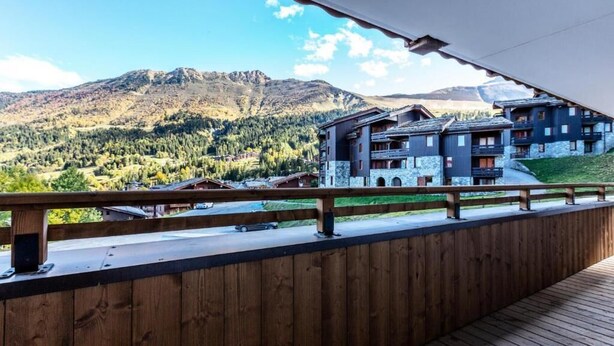 A wooden balcony overlooking a mountainous landscape with a multi-story building in the background. - Valmogrange E4 - 8 Persons - Luxury Apartment on the Piste (Les Avanchers-Valmorel)
