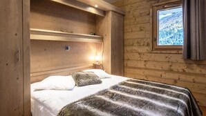 A wooden cabin room with a bed, a window with a view of a snowy landscape, and a shelf above the bed. - Valmogrange E4 - 8 Persons - Luxury Apartment on the Piste (Les Avanchers-Valmorel)