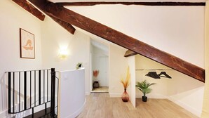 A staircase with a wooden beam, a black metal railing, and a white wall with a framed picture. - Charming Duplex in Marais for 2 People (Paris)