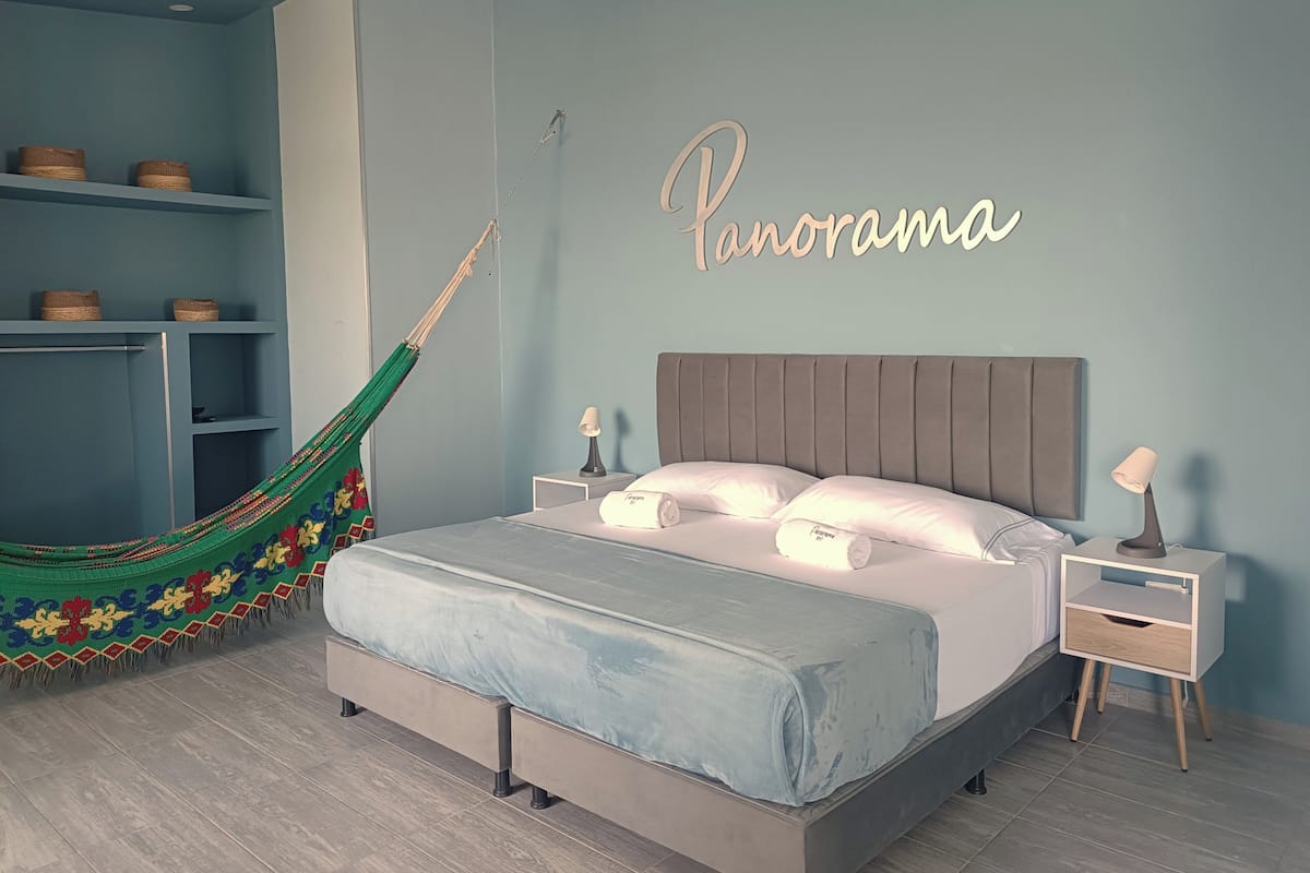 Un dormitorio con cama, mesitas de noche, una hamaca y un estante en la pared con cestas.